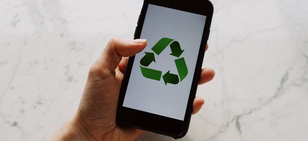 A close-up of a hand holding a smartphone with a recycling symbol on the screen, promoting sustainability and eco-consciousness.